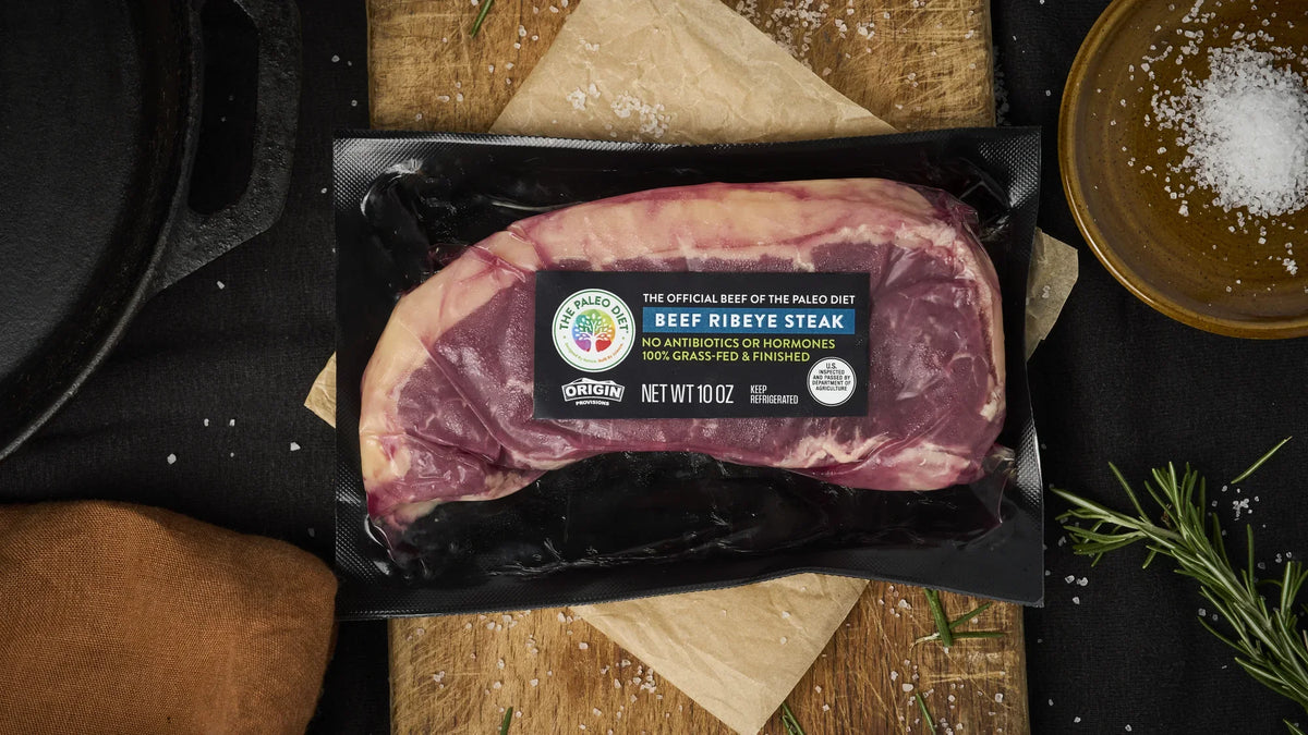 Origin Provisions ribeye steak beside a cast-iron skillet with rosemary and garlic