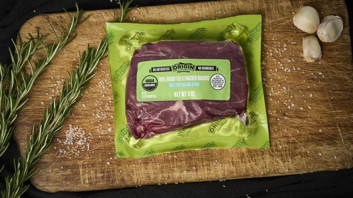 Origin Provisions top sirloin steak on a wooden board with rosemary and garlic