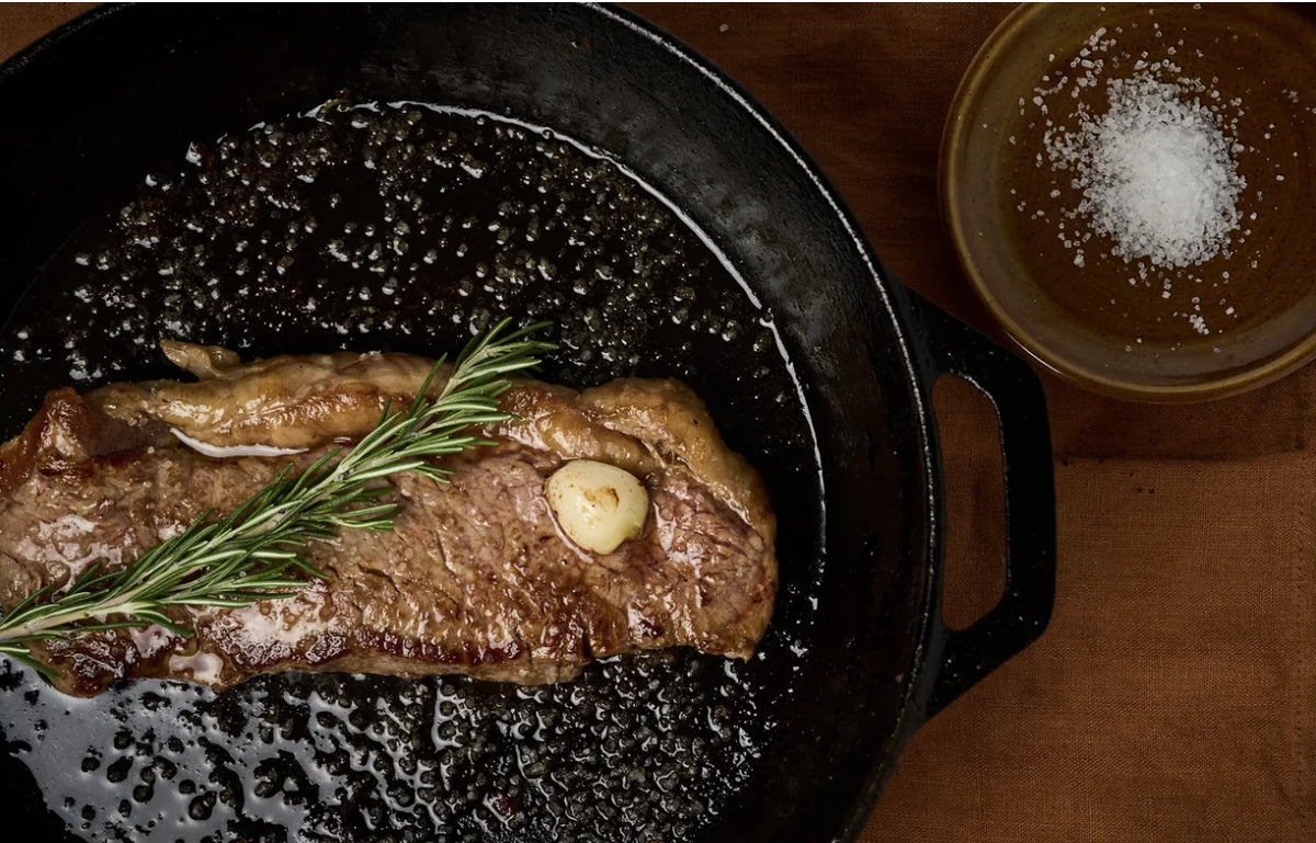 Steak searing in a cast-iron pan with rosemary and garlic