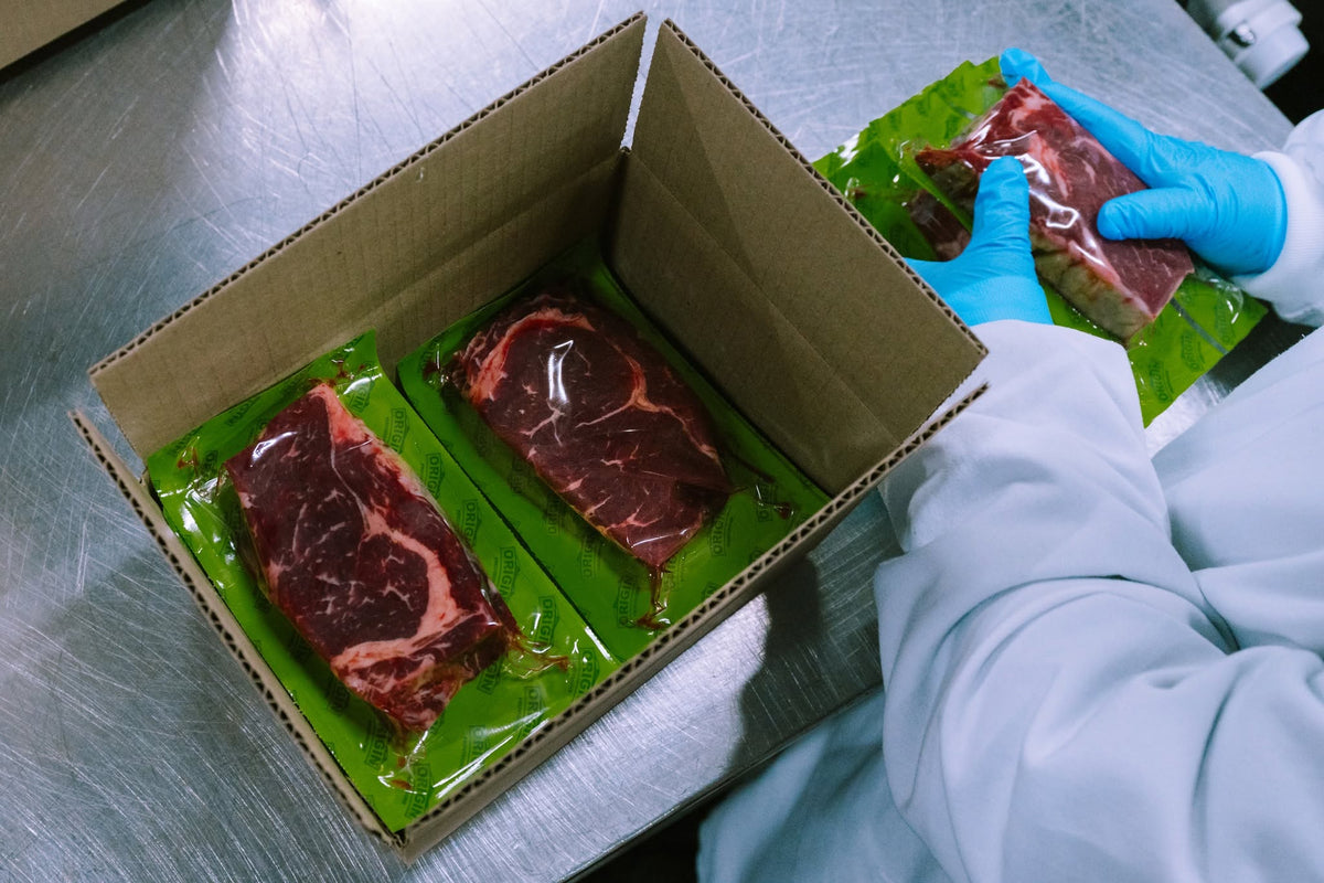 Gloved hands packing vacuum-sealed beef into a shipping box